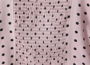 Détail de tissu rose froncé à pois noirs sur le haut à manches bouffantes et col carré