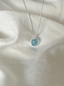 Macro detail of oval aquamarine pendant with silver bezel setting on woven texture