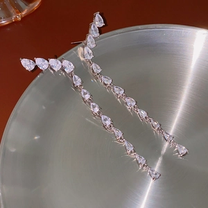 Close-up of dangling silver drop earrings featuring pear-cut cubic zirconia in a metal tray