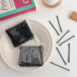 Detailed view of bulk black metal bobby pins in retail packaging on a white desk