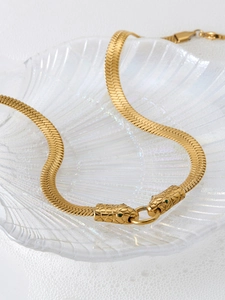Detail view of gold stainless steel snake head necklace with green eyes on glass tray