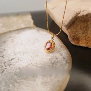 Detail of oval red gemstone pendant on a gold plated necklace with natural stone background