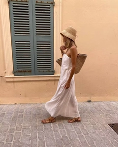 Close-up of a white pleated maxi dress paired with a straw sun hat and woven tote bag