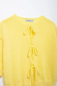 Detail of soft yellow mohair cardigan featuring three delicate bow tie closures at the front