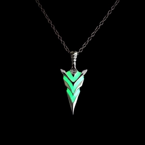 Macro shot of silver arrow pendant with glowing green fluorescent core on black background