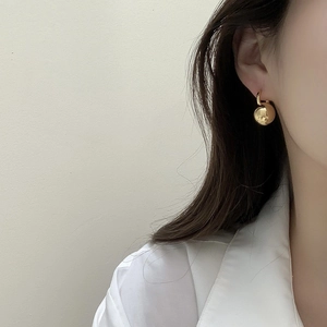 Detailed view of a woman wearing polished gold ball drop earrings with a minimalist design