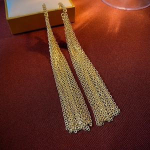 Detail shot of golden triangular tassel earrings with mesh chain texture on red fabric