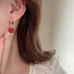 Detailaufnahme des vergoldeten Creolen-Ohrrings mit rotem Perlenanhänger am Model