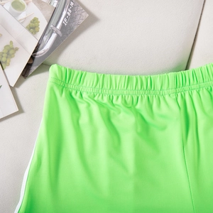 Detail of neon green sports shorts featuring elastic shirred waist and side white stripes
