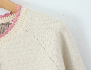 Detail of knit cardigan neckline with pink wavy trim and beige textured fabric on hanger