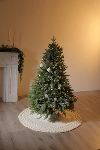 Close-up of a white knitted Christmas tree skirt with a double diamond pattern and warm lights