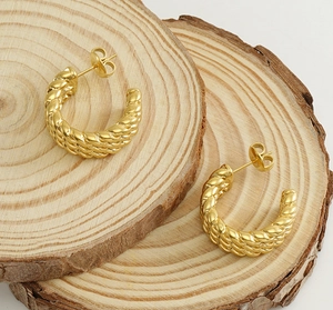 Macro shot of 18k gold-plated twisted C-shaped hoop earrings on natural wood base