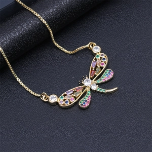 Detail view of a gold dragonfly pendant with colorful zircon stones on a black leather background