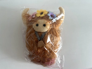 Close-up of Highland cow plush toy in packaging featuring long brown hair and floral detail
