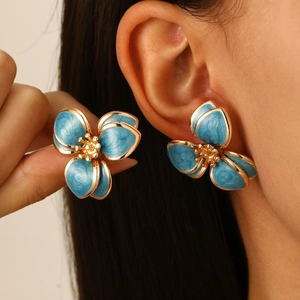 Detailaufnahme der blauen Blumenohrringe mit Goldrand und Mitte am Ohr eines Modells