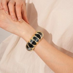 Macro detail of wide gold elastic bracelet with marbled black and grey stone inserts