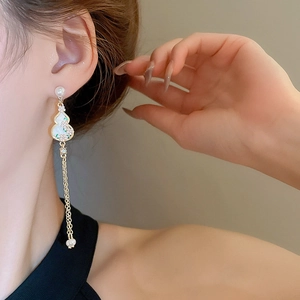 Detail of long tassel earrings with gourd motif, pearls, and gold finish on model