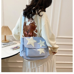 Close-up of light blue messenger bag with white plush star patches and adjustable strap