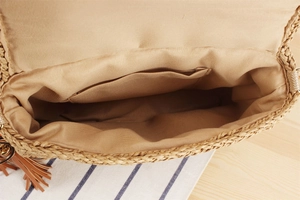 Detail view of woven straw bag with fabric lining, inner pocket, and leather tassel charm