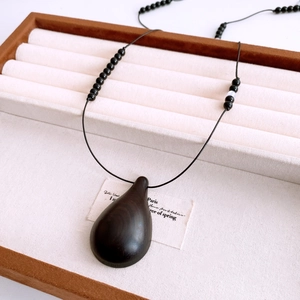 Close-up of teardrop dark wood pendant with smooth texture on a beige jewelry display