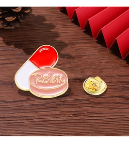 Detail of Relax enamel pill brooch with gold border on a dark wood background