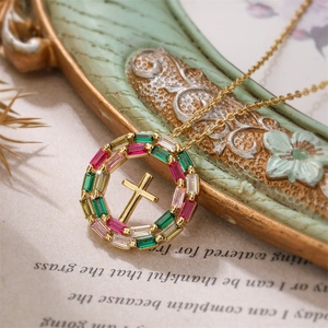 Détail d'un collier pendentif croix dorée serti de zircons colorés sur une chaîne fine