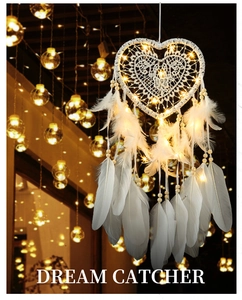 Macro detail of white heart-shaped dream catcher with glowing LED fairy lights and feathers