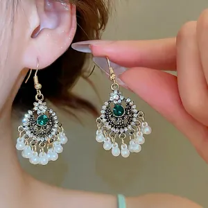 Orecchini pendenti vintage dorati con cristallo verde, strass e nappe di perle su modella