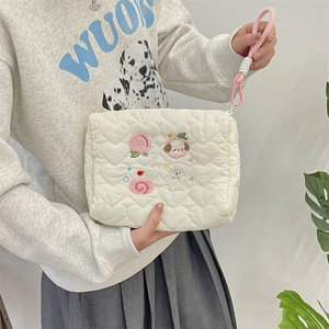 Detail of heart-quilted cream makeup bag with cute cartoon embroidery and pink wristlet