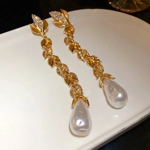 Detail of golden leaf earrings with shimmering rhinestones and teardrop pearl drops