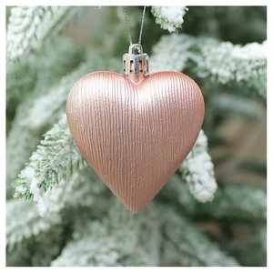 Detailed view of a rose gold heart ornament with ribbed texture on a snowy branch