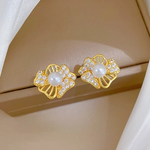 Macro shot of gold floral earrings with pearl and zircon inlay on soft beige box