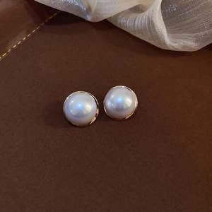Close-up of elegant round white pearl earrings with minimalist gold metal trim on leather
