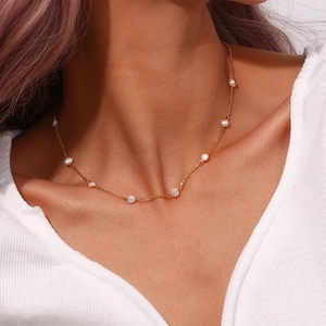 Close-up of a gold chain necklace featuring small white pearls on a model wearing white