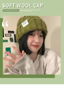 Detailed knit texture of green wool beanie with a white decorative patch on the brim