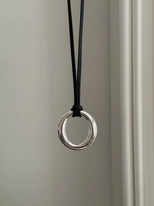 Close-up of polished silver circle pendant with black leather cord on a neutral wall