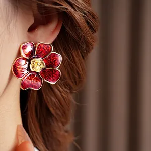Pendientes de flores rojas vintage con bordes dorados y textura en una modelo