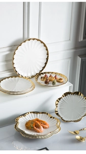 Detail of scallop-shaped white ceramic plates with elegant gold rim in a luxury setting