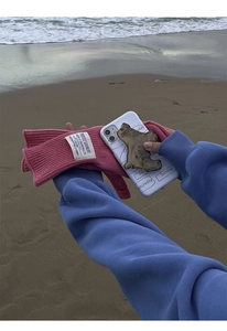 Detailed shot of pink wool knit gloves with a bear phone case on a sunny beach background