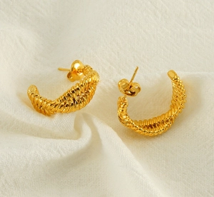 Macro detail of gold-plated twisted rope hoop earrings on beige fabric background