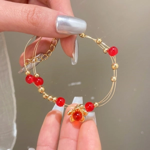 Dettaglio di un bracciale dorato vintage multifilo con perline rosse e ciondolo a fiore