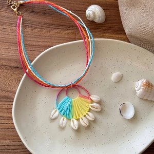 Close-up detail of a colorful woven raffia necklace with white cowrie shells on a plate