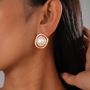 Detail view of a model wearing a gold flower earring with white pearl inlay