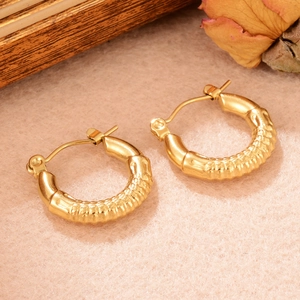 Détail de boucles d'oreilles créoles dorées texture bambou sur fond en feutre beige