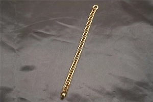 Dettaglio del bracciale a catena cubana dorata lucida su seta grigia elegante