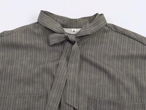 Detail of grey-green striped shirt featuring tie-neck bow and dual front pockets