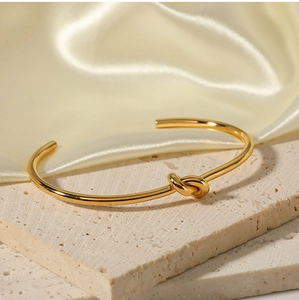 Dettaglio del bracciale rigido a nodo placcato oro 18K su superficie in pietra crema