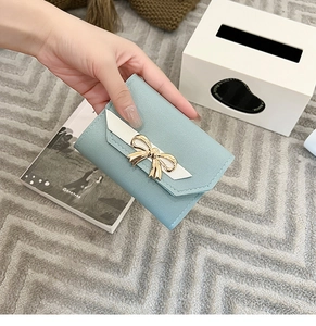 Close-up of light blue leather short wallet with a gold bow buckle and contrast white trim