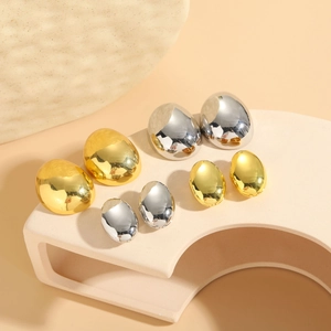 Polished egg-shaped metal hoop earrings in gold and silver finish on a display