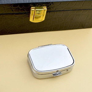 Portable silver rectangular metal pill box with rounded edges on a warm beige background